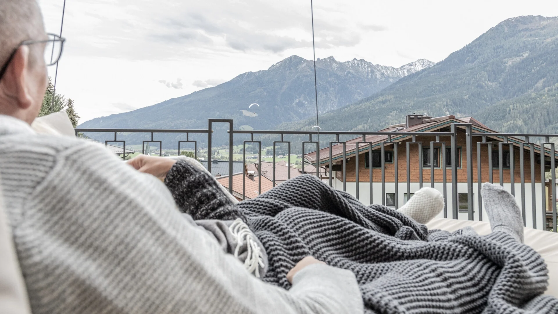Baumhaus Person entspannt mit Decke auf Balkon mit Bergblick und Paragleitern