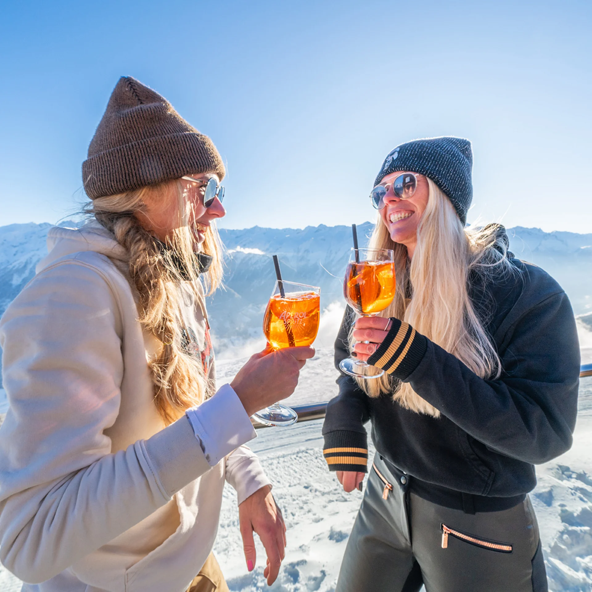 Skifahren Zwei Frauen genießen Aperol Spritz auf einer sonnigen Bergterrasse im Schnee