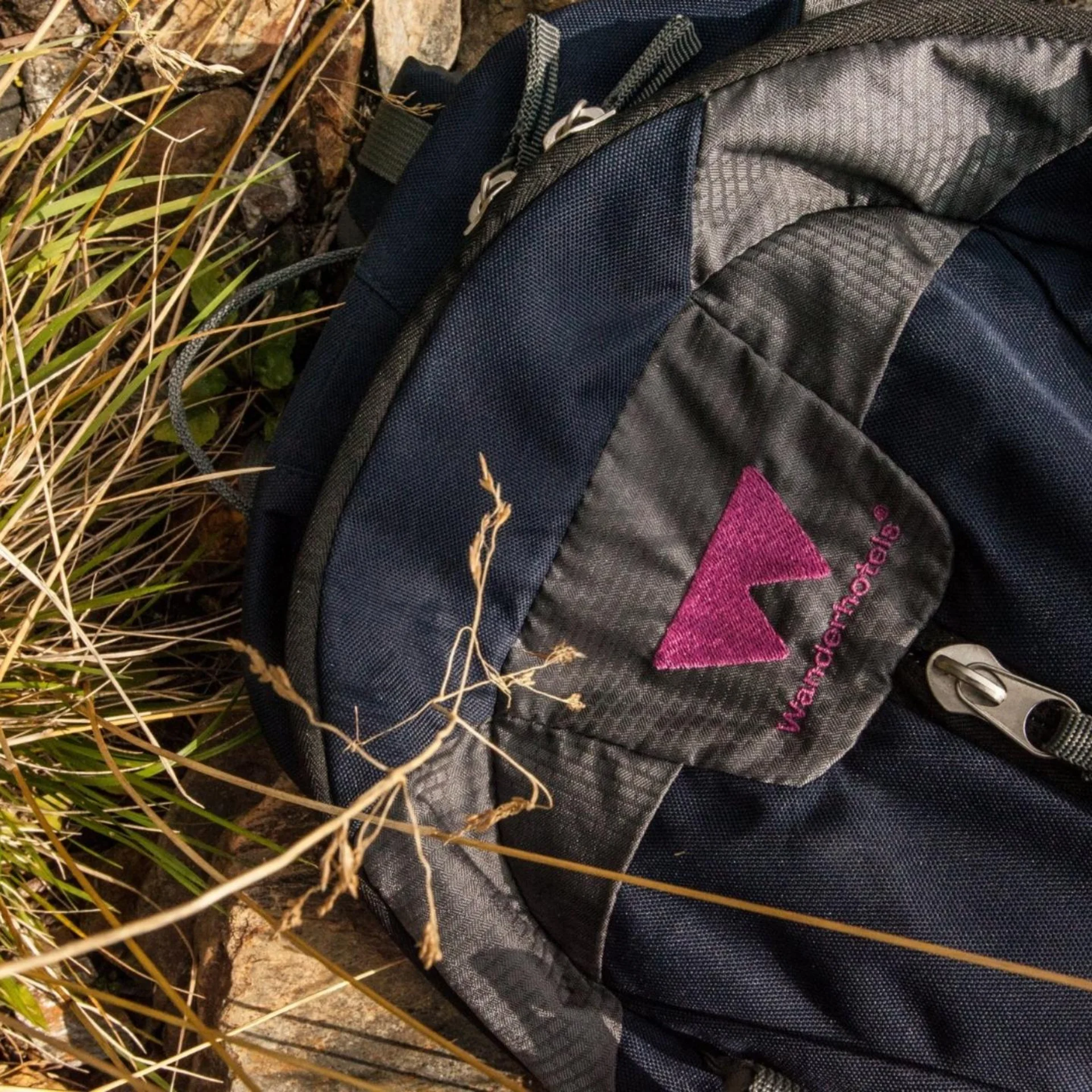 Wanderhotel Blauer und grauer Rucksack mit lila Logo liegt im Gras