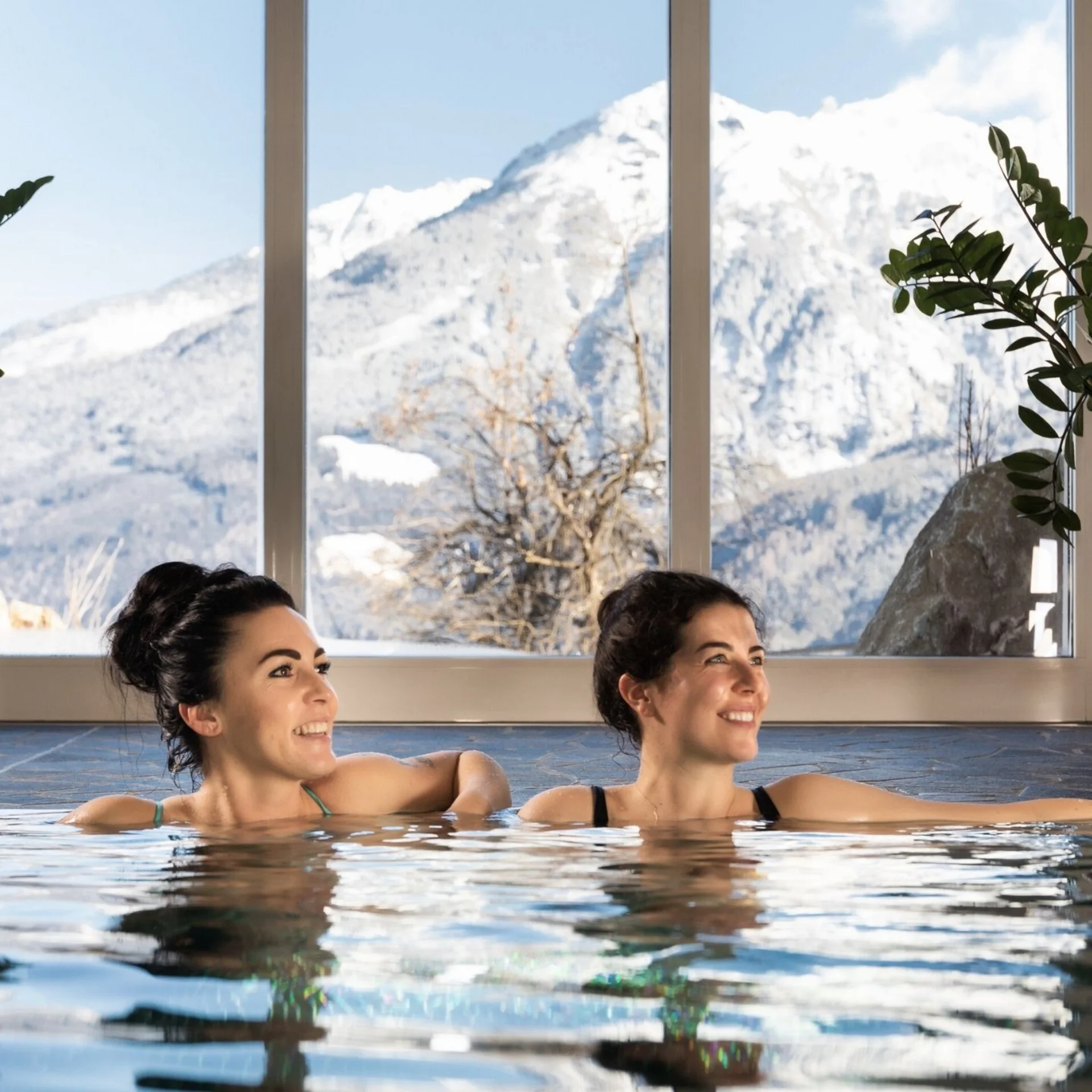Wellness Zwei Frauen entspannen sich im Hallenbad mit Blick auf schneebedeckte Berge