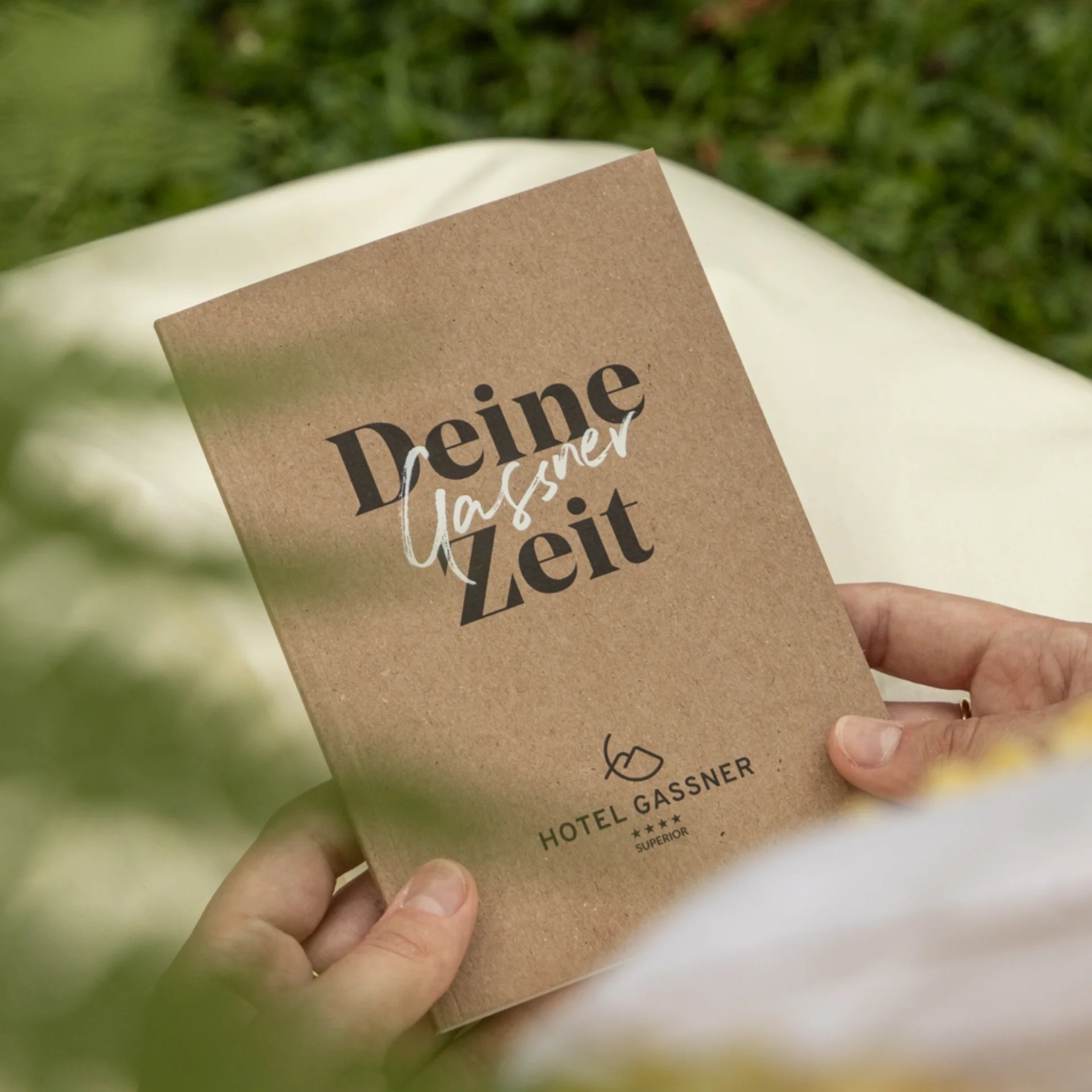 Downloads Person hält Broschüre mit Schriftzug Hotel Gassner in der Natur