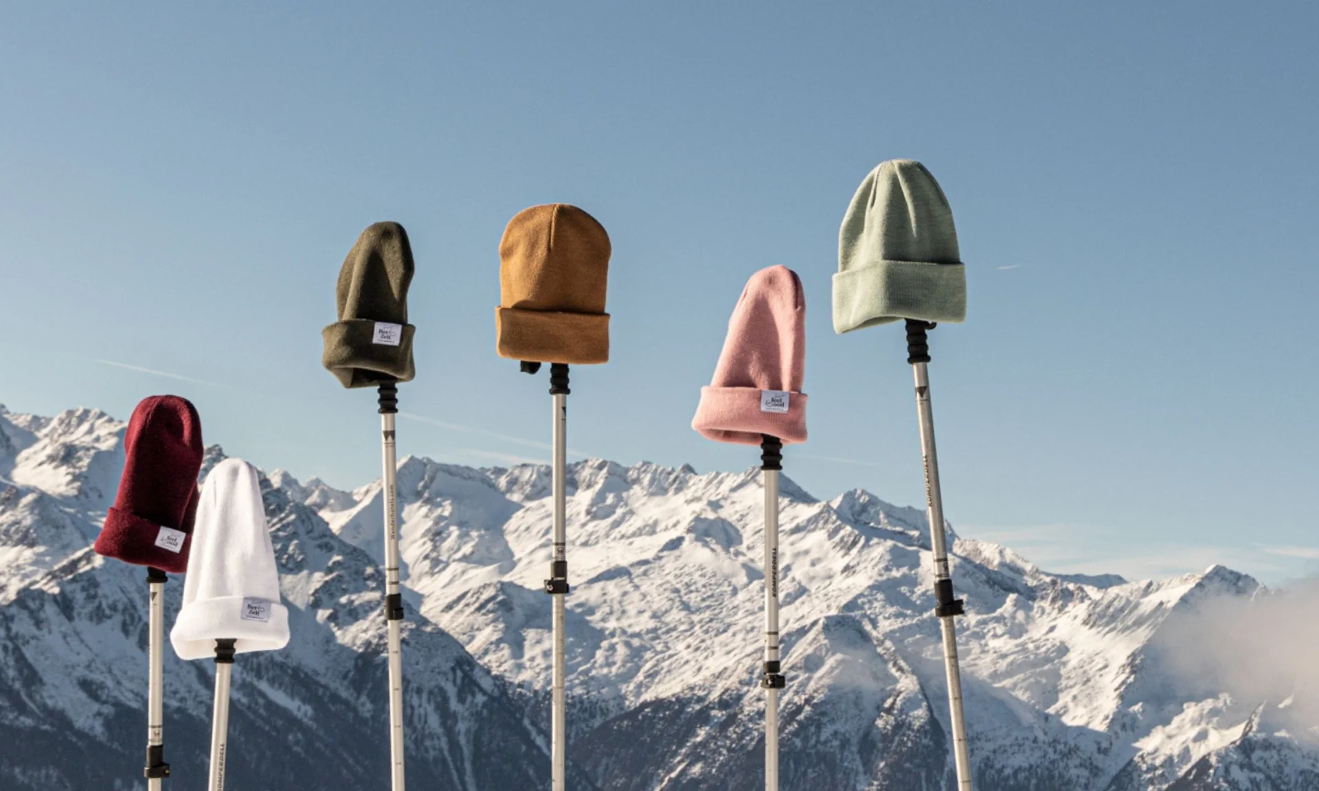 Home Wintermützen auf Stöcken vor schneebedeckten Bergen und blauem Himmel