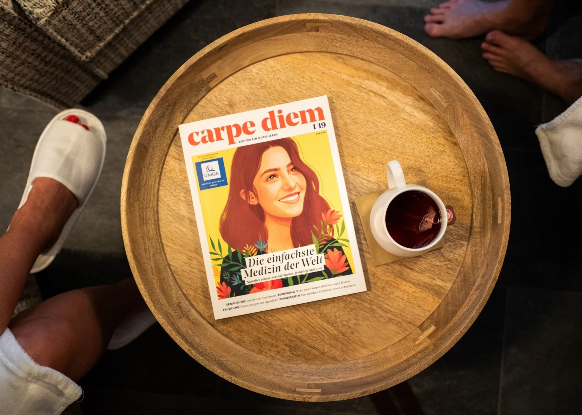 Jobs Holztisch mit Magazin Carpe Diem und Tasse Tee, Menschen barfuß und in Hausschuhen