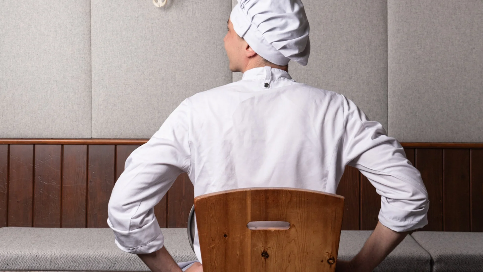 Lehrlingsausbildung Koch in weißer Kleidung sitzt auf einem Holzstuhl, hält Kochlöffel, Blick auf Wandschädel