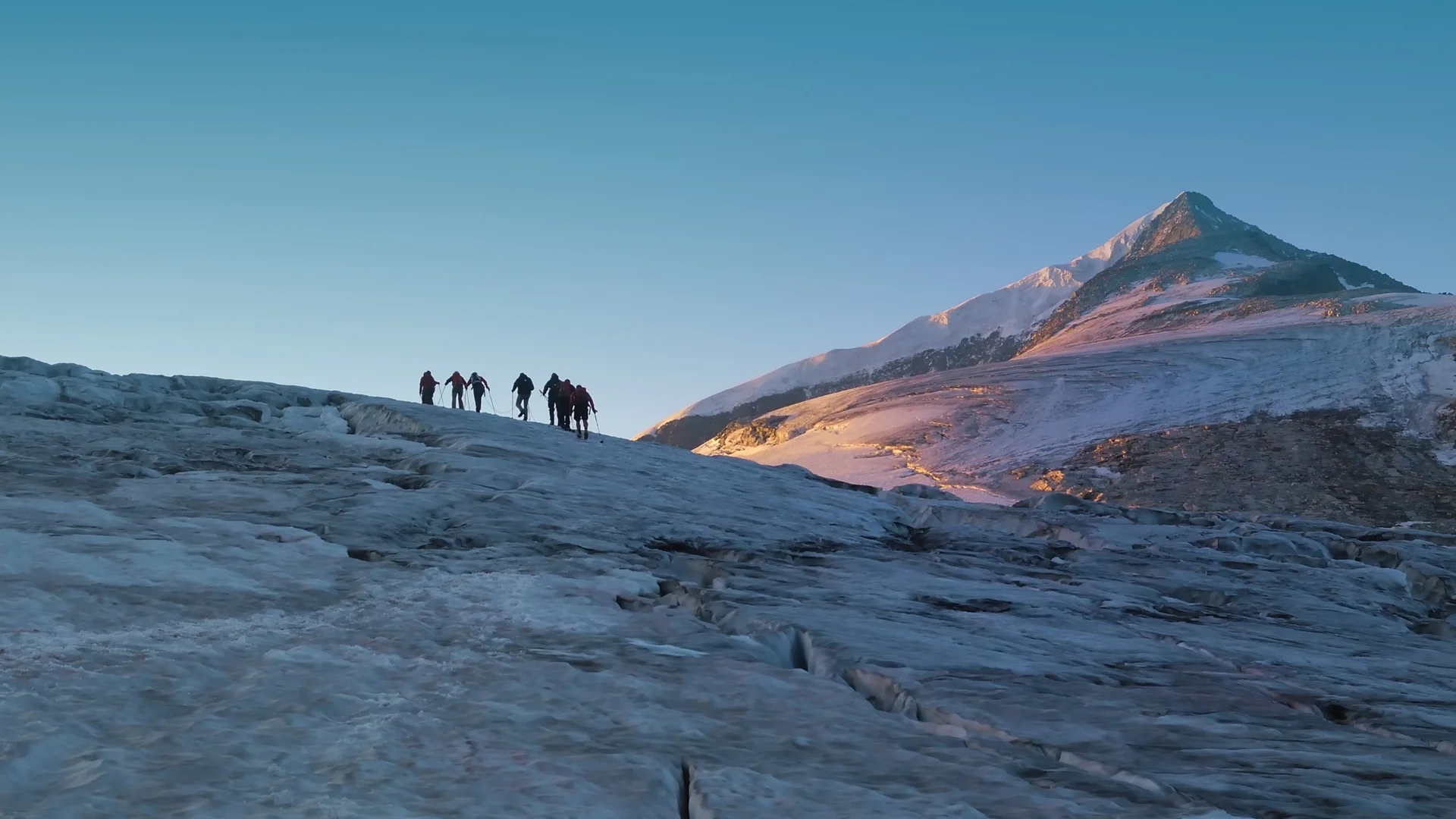 Wanderhotel Gruppe von Bergsteigern auf eisigem Gletscher vor spitzem Berggipfel im Morgenlicht