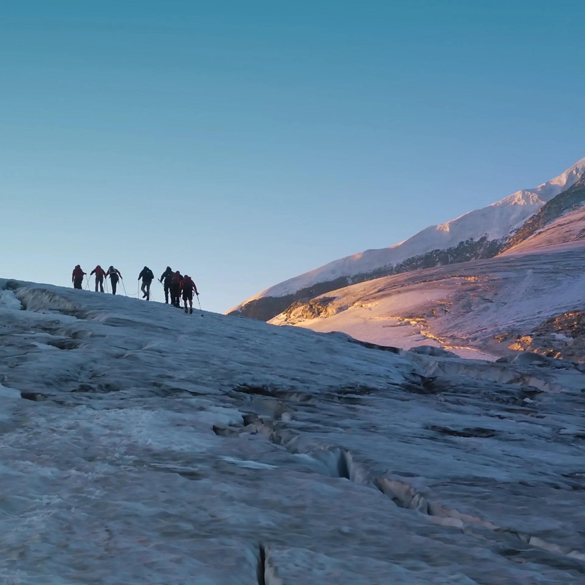 Großvenediger Gruppe von Bergsteigern auf eisigem Gletscher vor spitzem Berggipfel im Morgenlicht