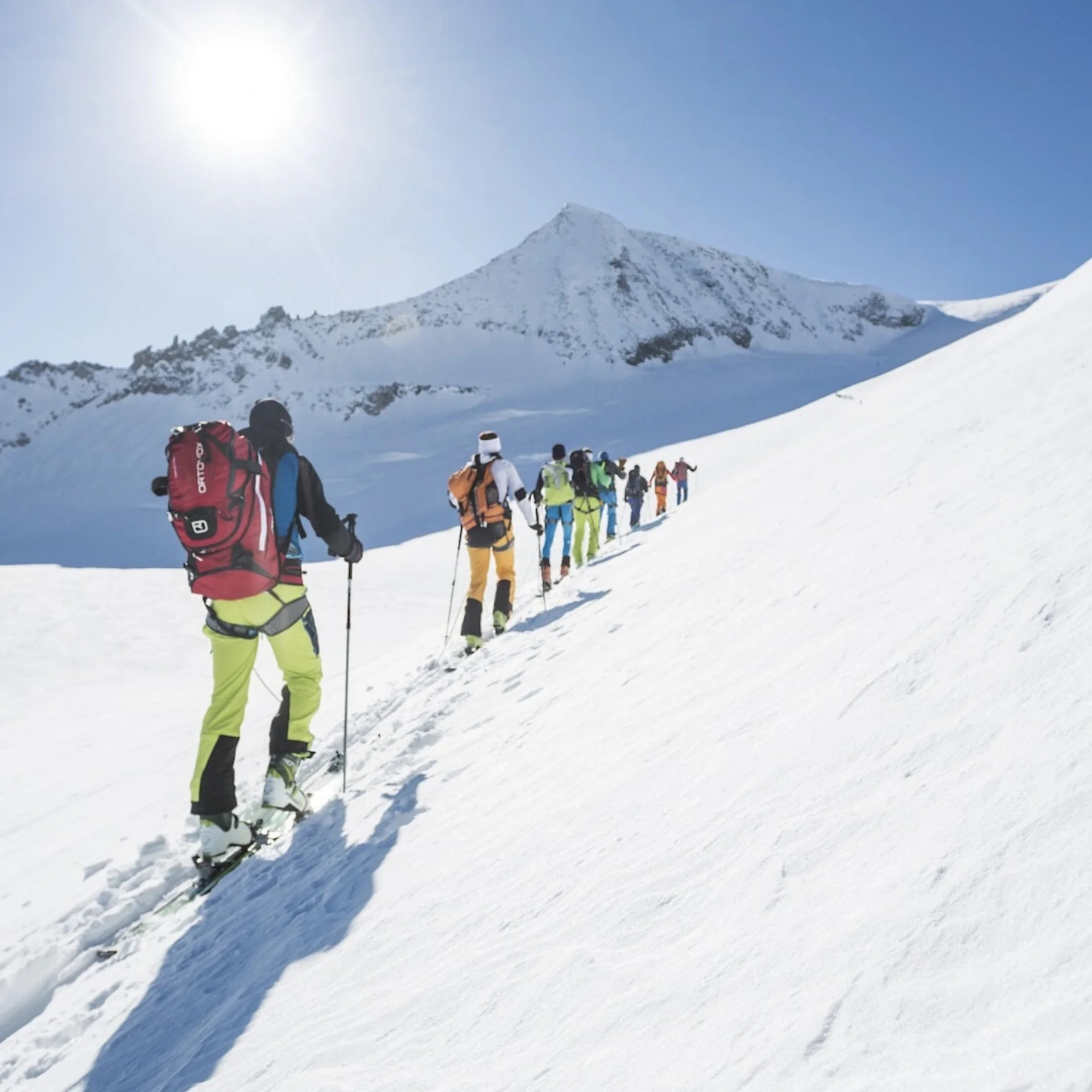 Abseits der Piste Gruppe von Skitourengehern steigt bei sonnigem Wetter einen schneebedeckten Berg hinauf