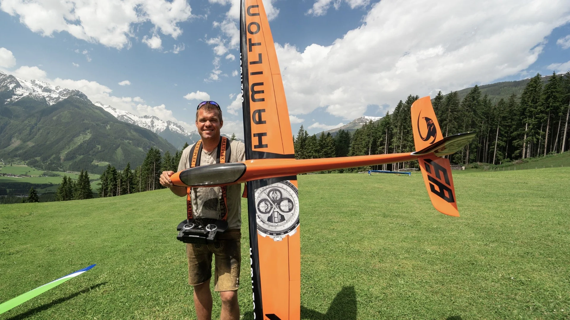Modell- und Hangfliegen Mann hält ferngesteuertes Modellflugzeug vor Bergkulisse mit grünem Gras und Wald