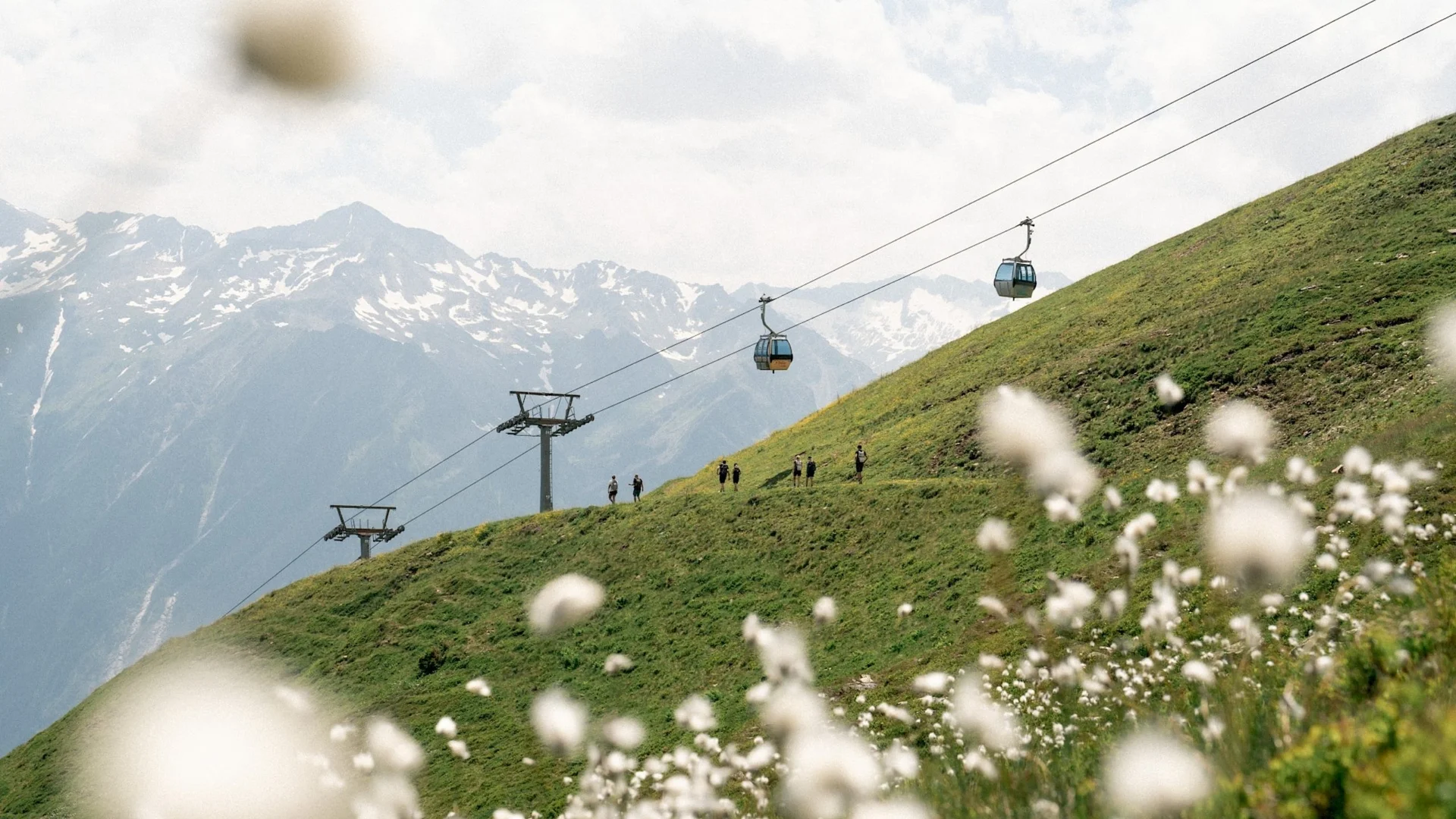 Nationalpark Sommercard Seilbahn über grüne Alpenwiese mit Wanderern und schneebedeckten Bergen im Hintergrund