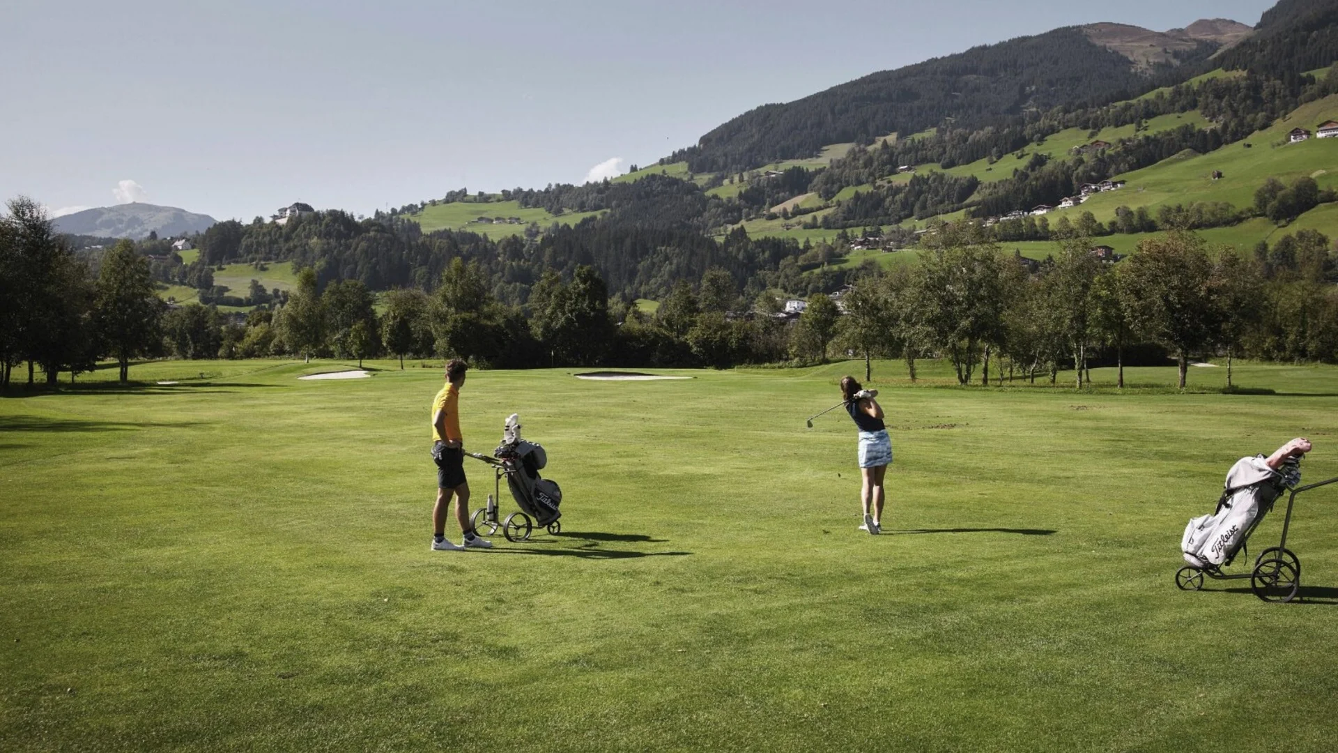 Golfen Zwei Golfer auf einem grünen Golfplatz mit Bergen im Hintergrund