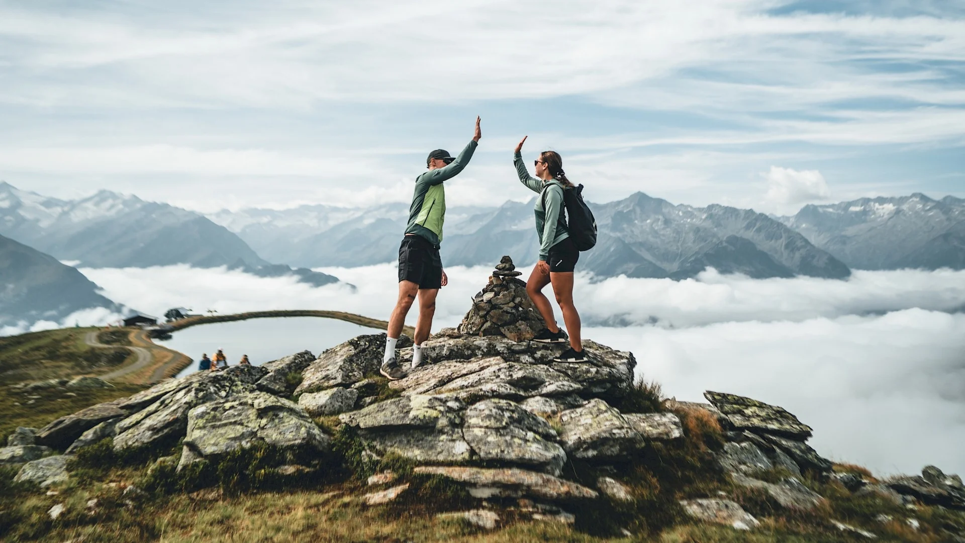 Benefits im Hotel Zwei Wanderer geben sich auf Berggipfel High-Five mit Alpen und Wolken im Hintergrund
