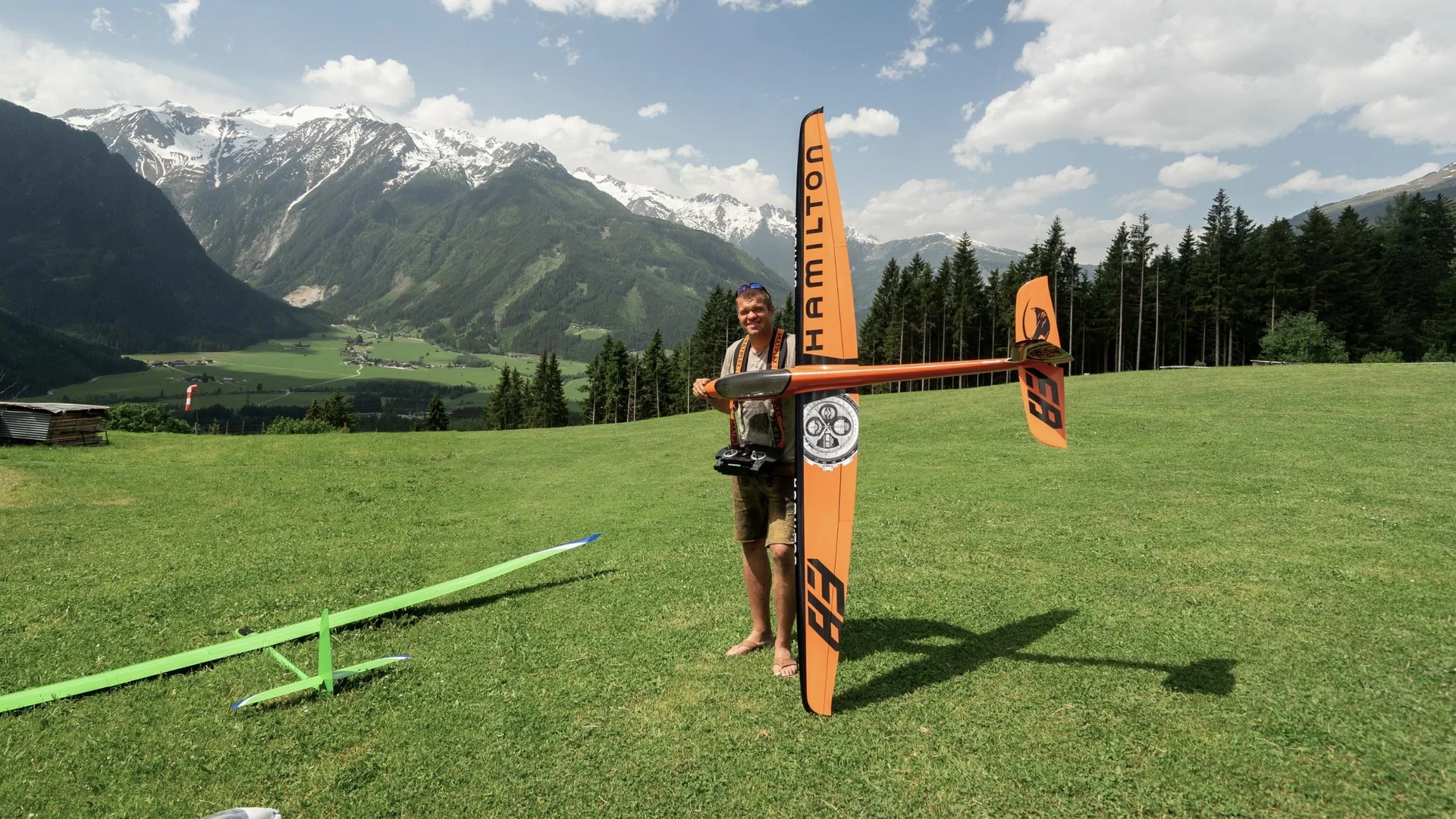 Modell- und Hangfliegen Mann hält ferngesteuertes Modellflugzeug auf grüner Wiese vor Bergkulisse