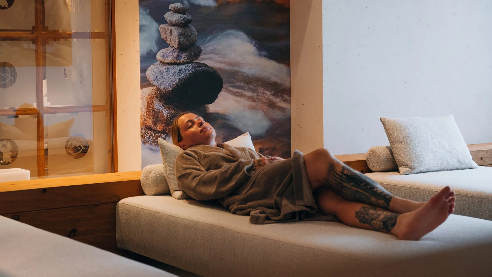 Saunawelt Frau entspannt auf Liege in einem Spa mit Steinskulptur im Hintergrund