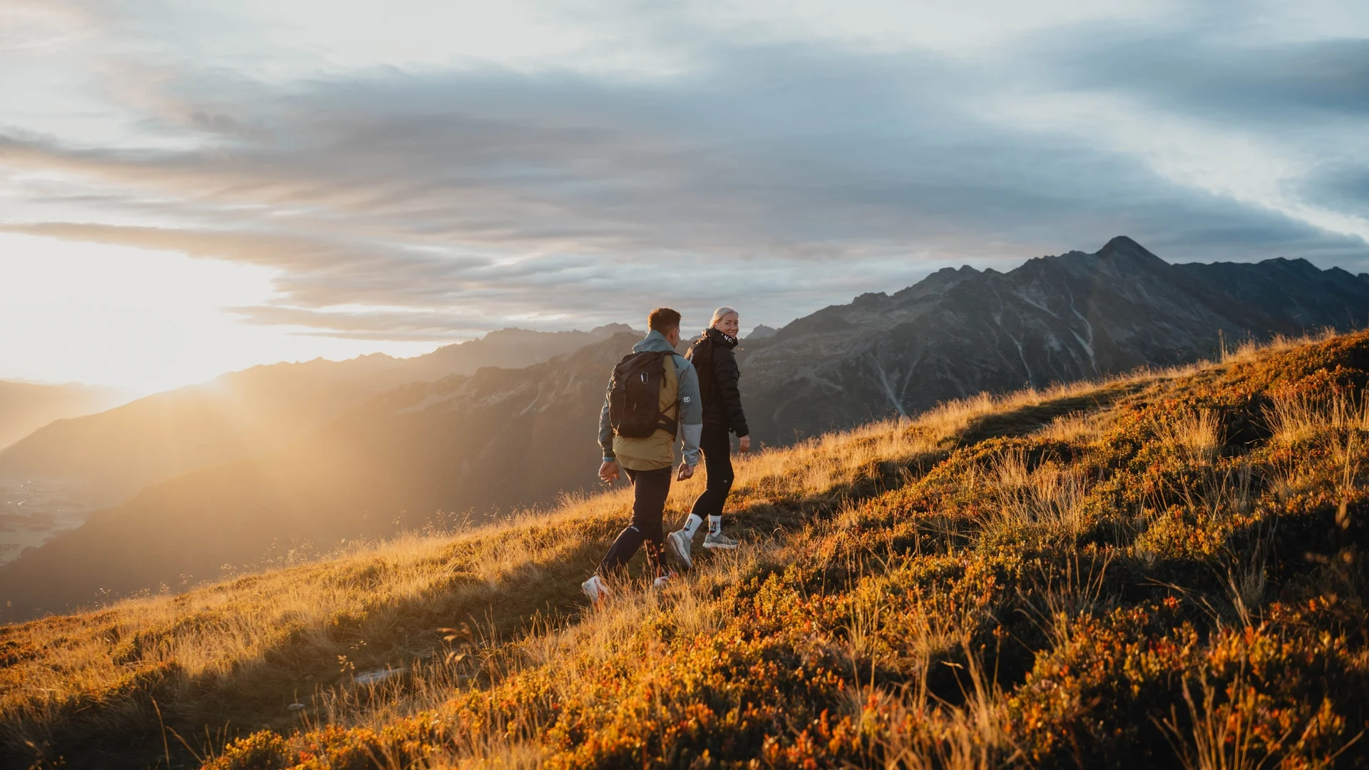 Wandern Zwei Wanderer auf einem sonnenbeschienenen Berghang bei Sonnenuntergang