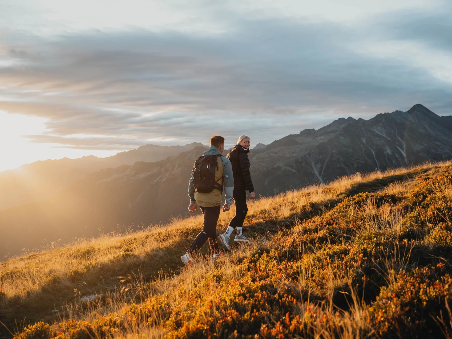 Biken Zwei Wanderer auf einem sonnenbeschienenen Berghang bei Sonnenuntergang