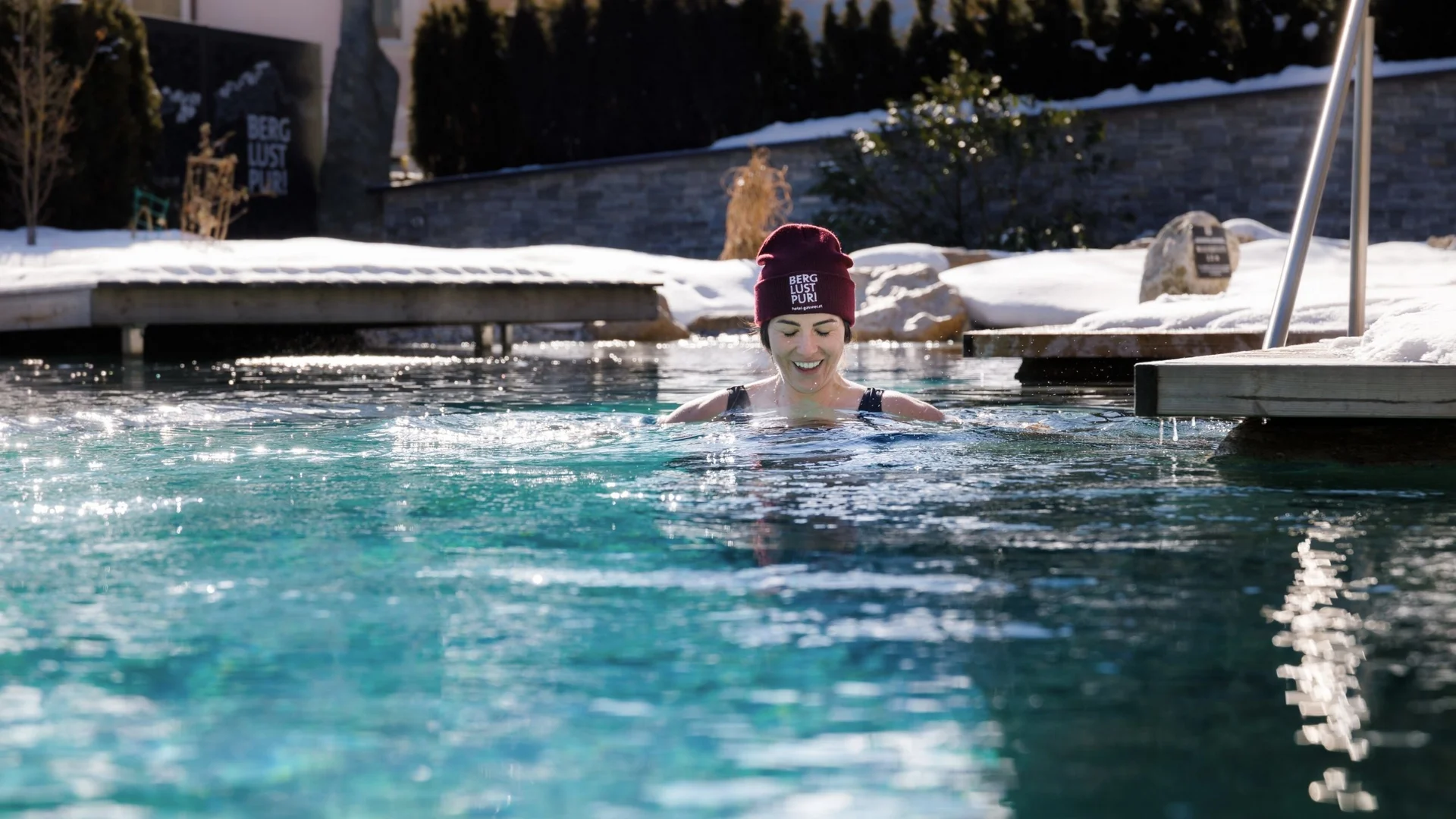 Saunawelt Frau im Winter draußen im Pool mit Mütze und Schnee im Hintergrund