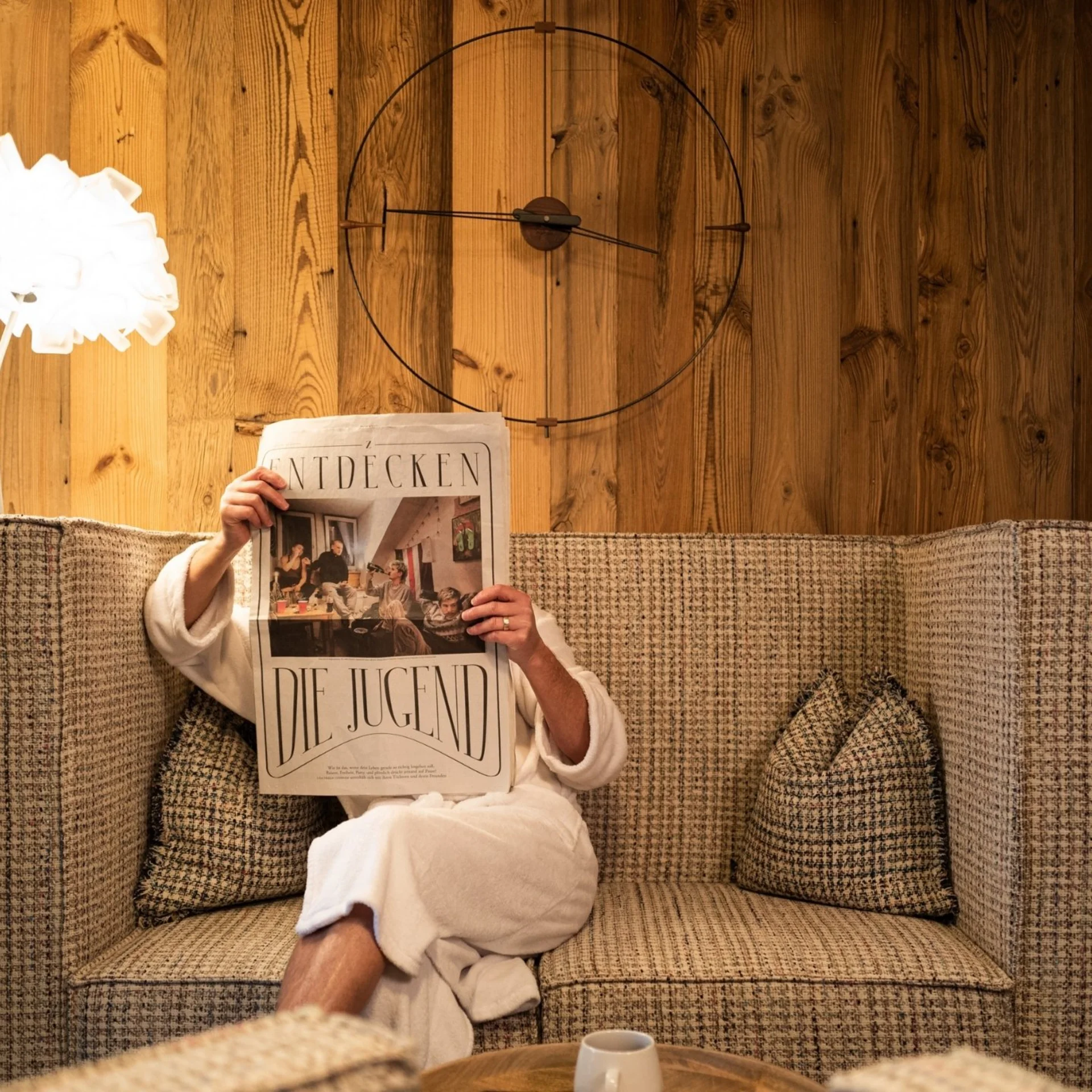 Wellness Person im Bademantel liest auf Sofa eine Zeitung in gemütlichem Raum
