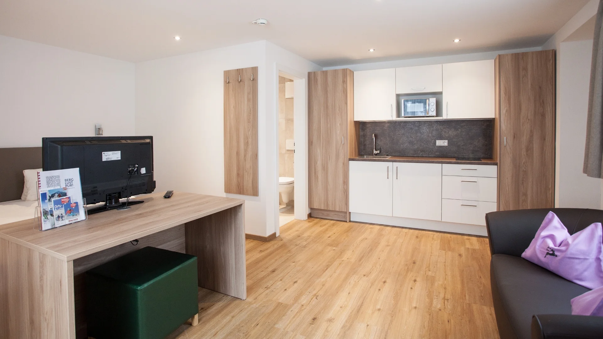 Benefits im Hotel Kleine moderne Küchenzeile und Wohnbereich mit Tisch, TV und Sofa im Apartment