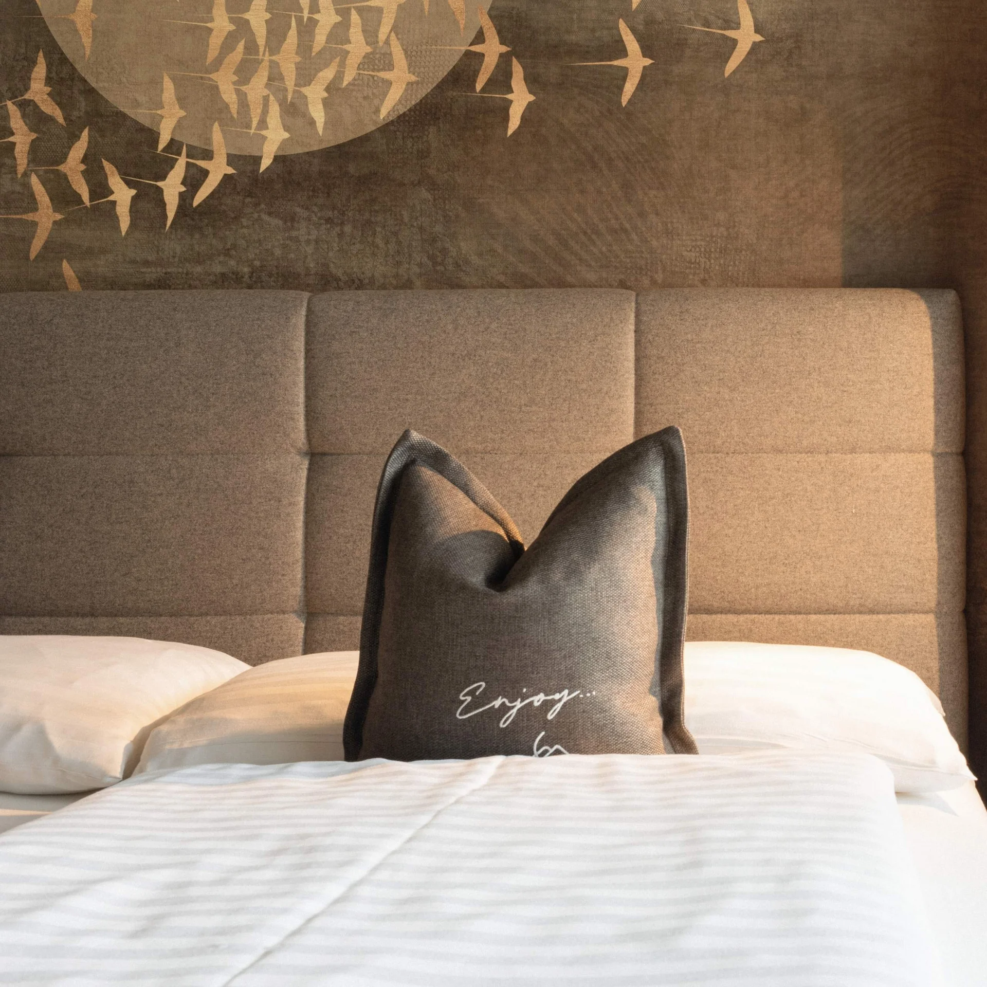 WORK FOR US Gemütliches Bett mit braunem Kopfteil und dekorativem Kissen vor Wand mit Vogelmotiv