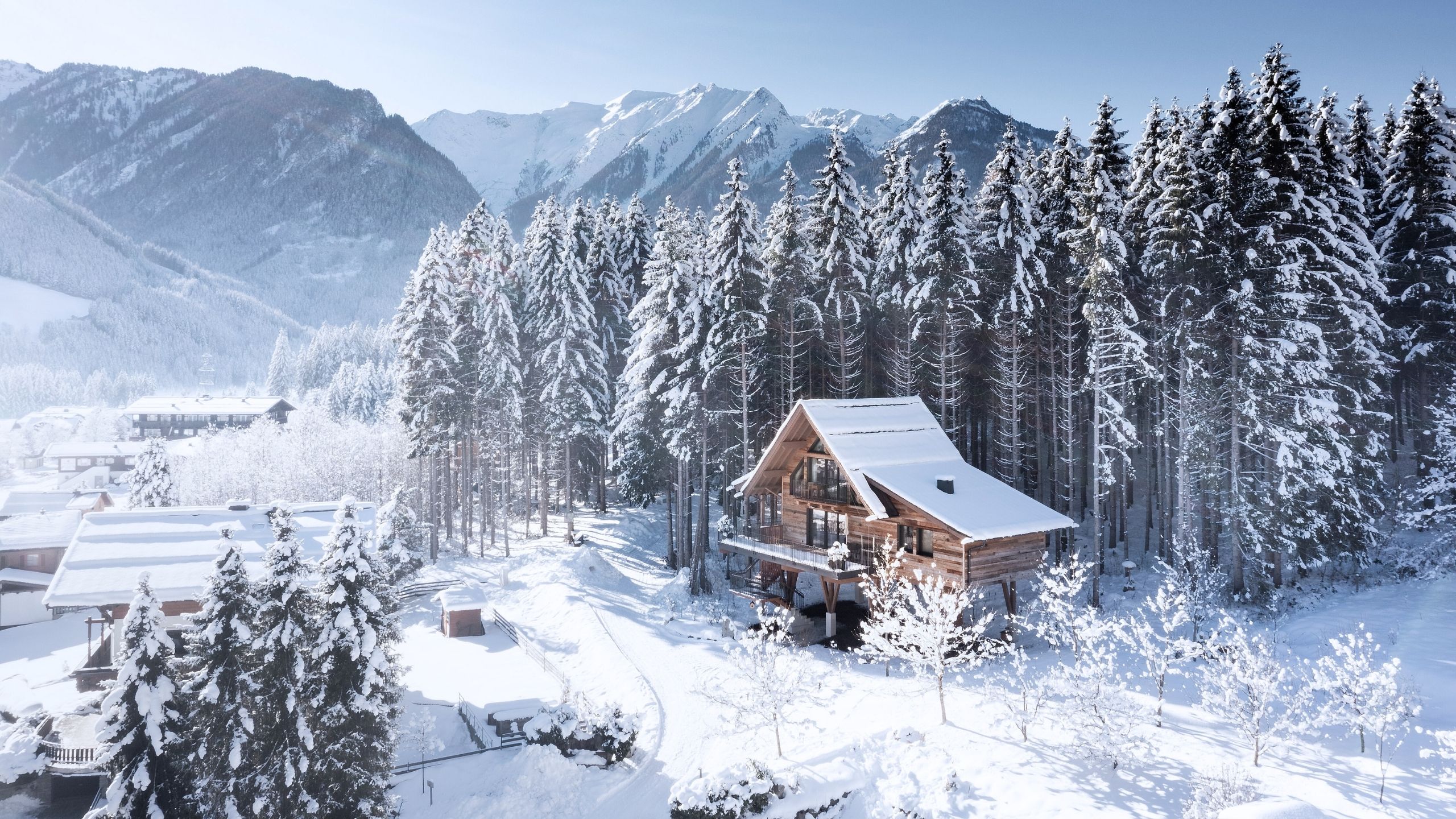 Baumhaus Verschneites Holzhaus am Waldrand vor Bergkulisse im Winter