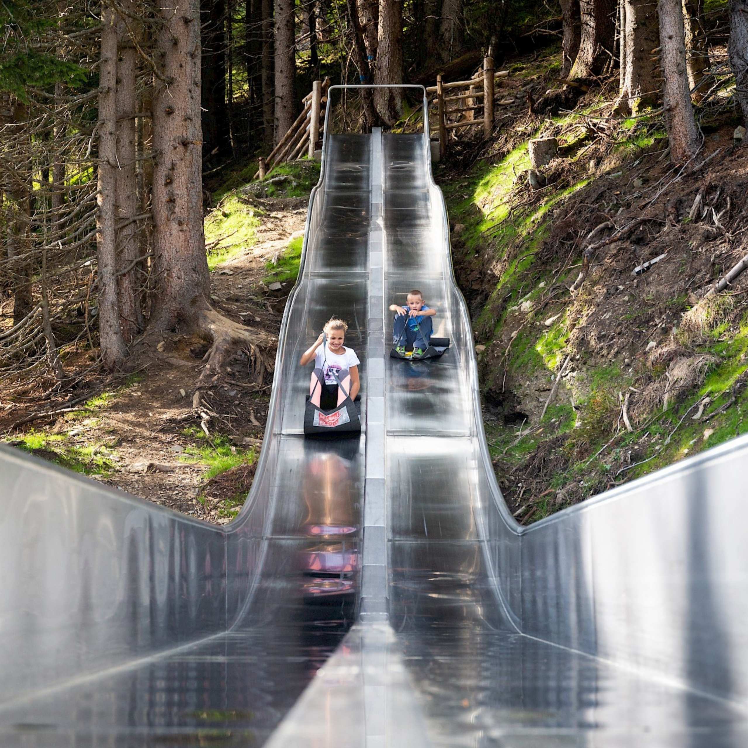 Ausflugstipps Zwei Kinder rutschen auf Matten eine Doppelrutsche aus Metall in der Wildkogel-Arena hinunter