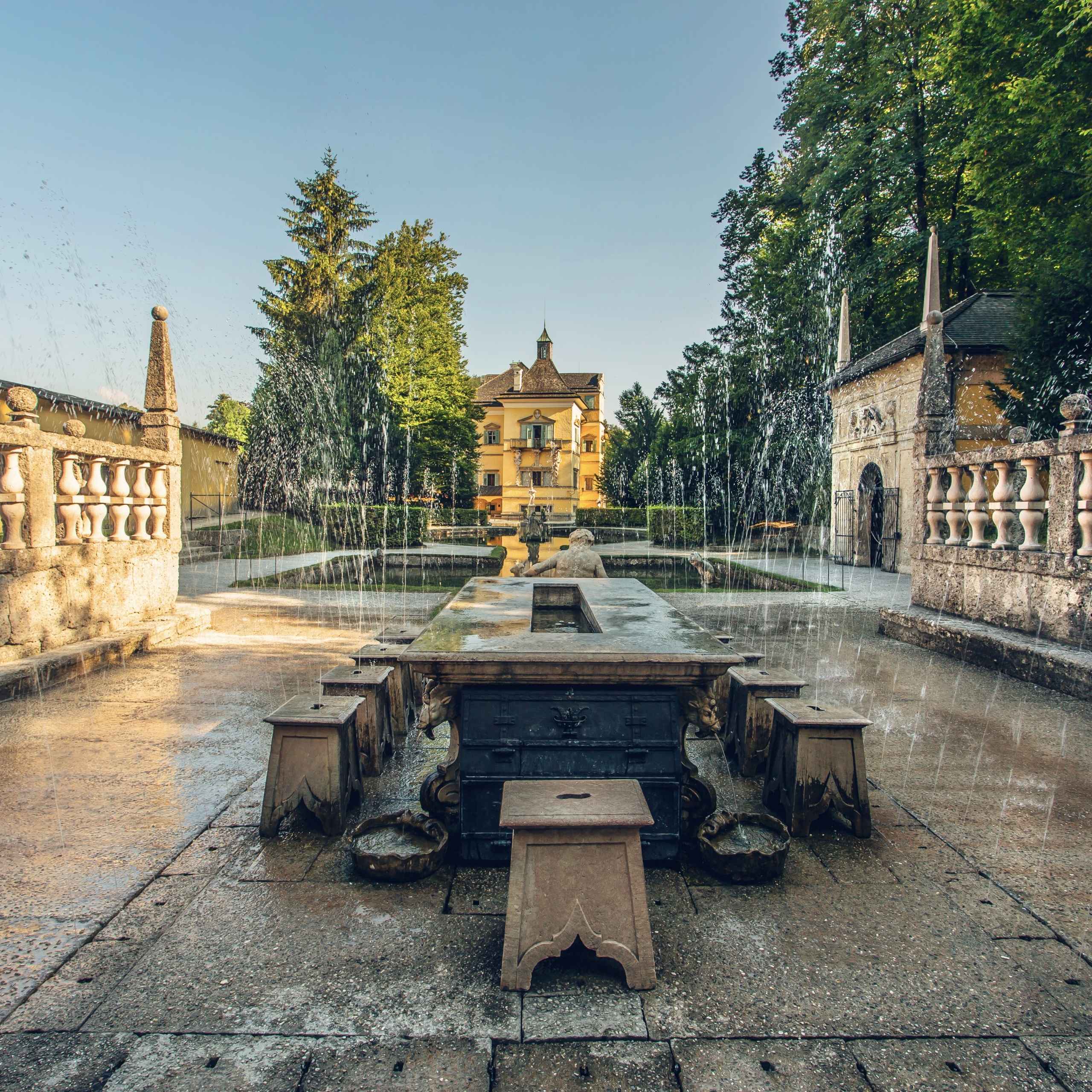 Ausflugstipps Antiker Springbrunnen mit Wasserspielen vor einem historischen Gebäude im Garten vom Schloss Hellbrunn in Salzburg