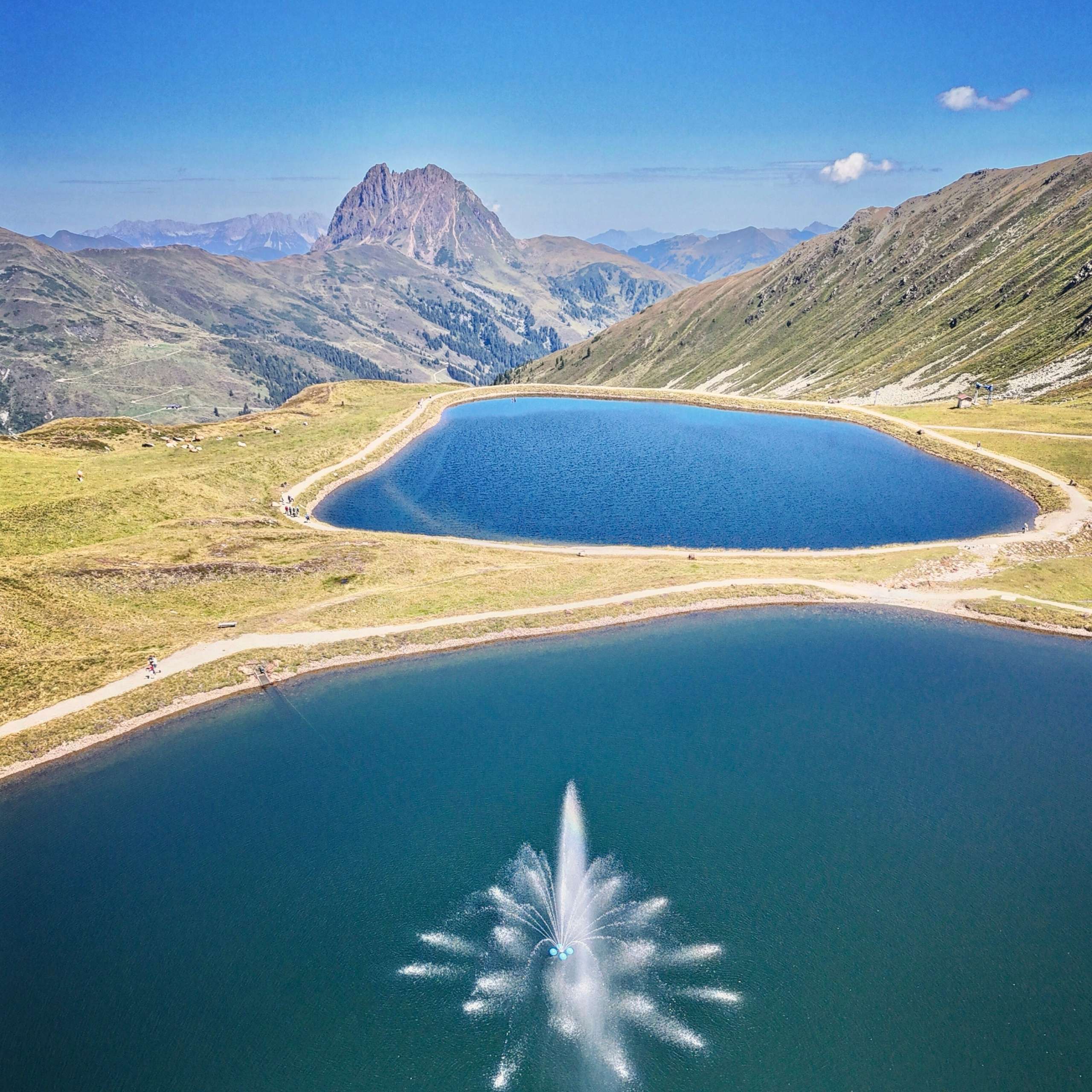 Ausflugstipps Zwei Alpenseen mit Springbrunnen vor Berglandschaft bei klarem Himmel