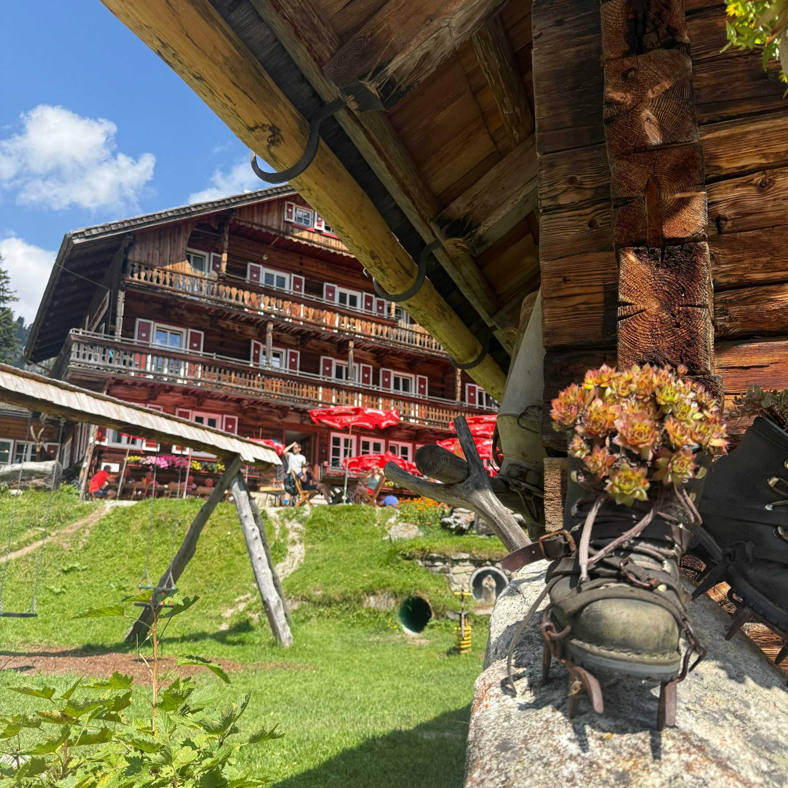 Ausflugstipps Altes Holzhaus mit Blumenschuhen und rotem Sonnenschirm im Garten