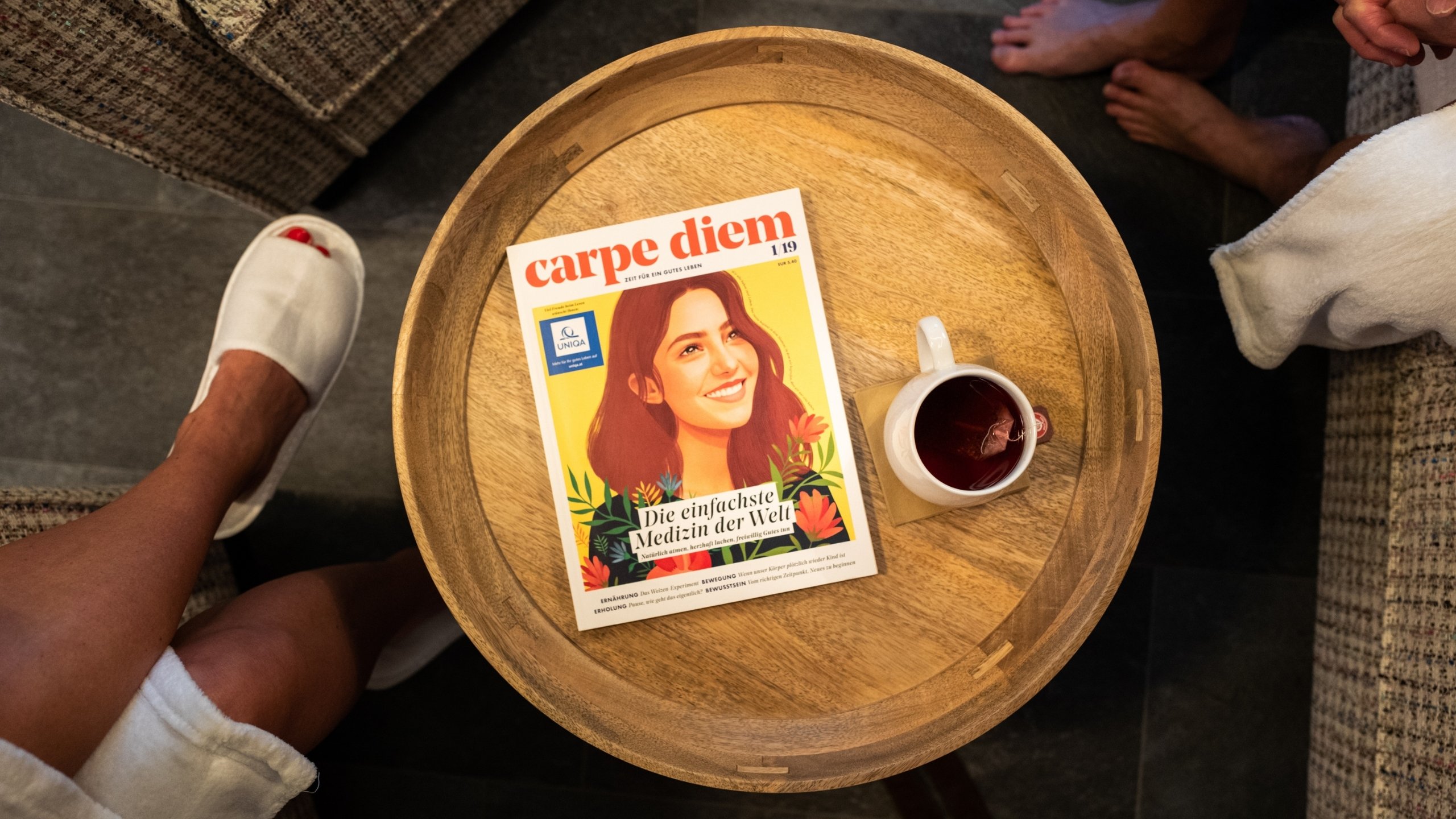 Saunawelt Holztisch mit Magazin Carpe Diem und Tasse Tee, Menschen barfuß und in Hausschuhen