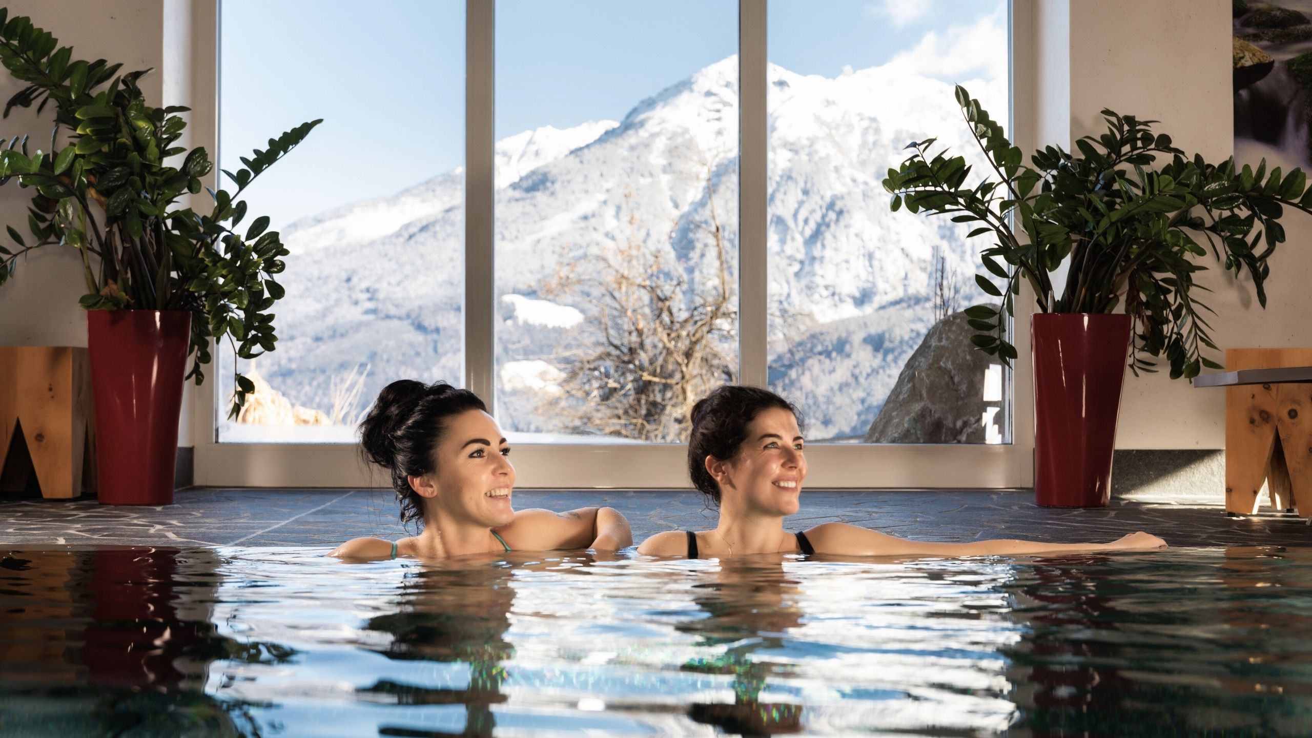 Wasserwelt Zwei Frauen entspannen sich im Hallenbad mit Blick auf schneebedeckte Berge