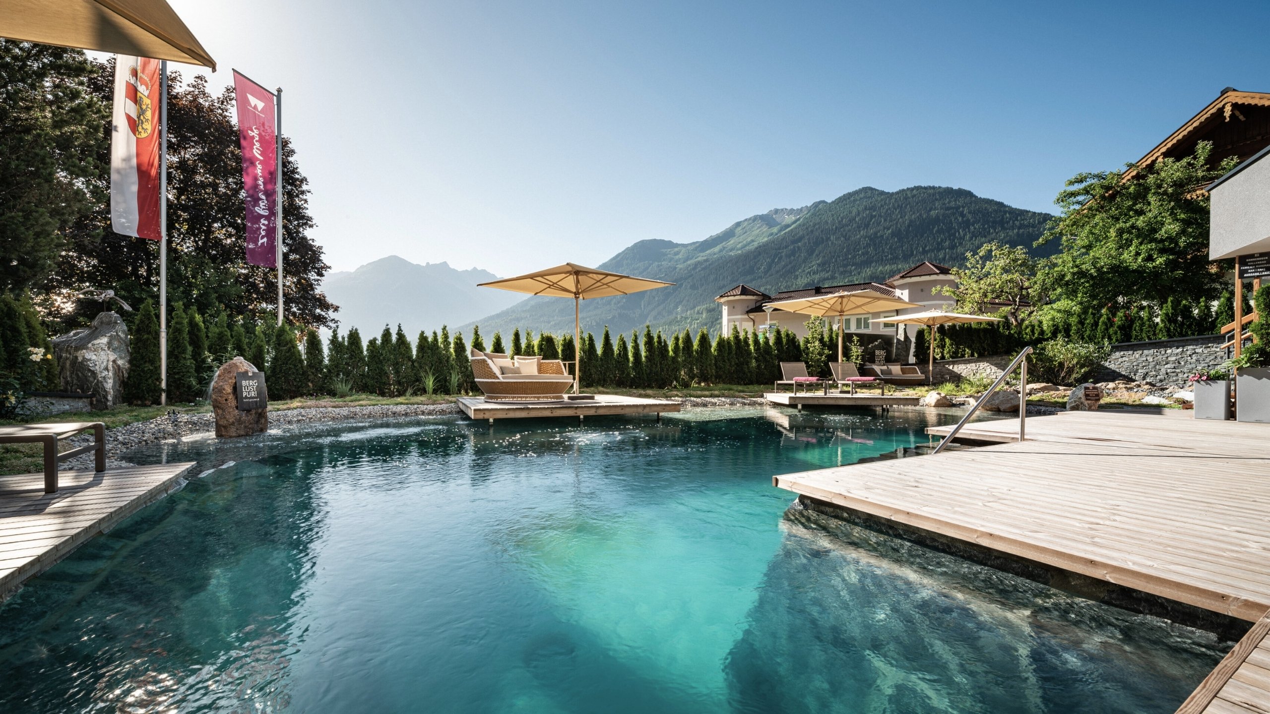 Wellness Außenpool mit Liegestühlen und Sonnenschirmen vor Bergkulisse