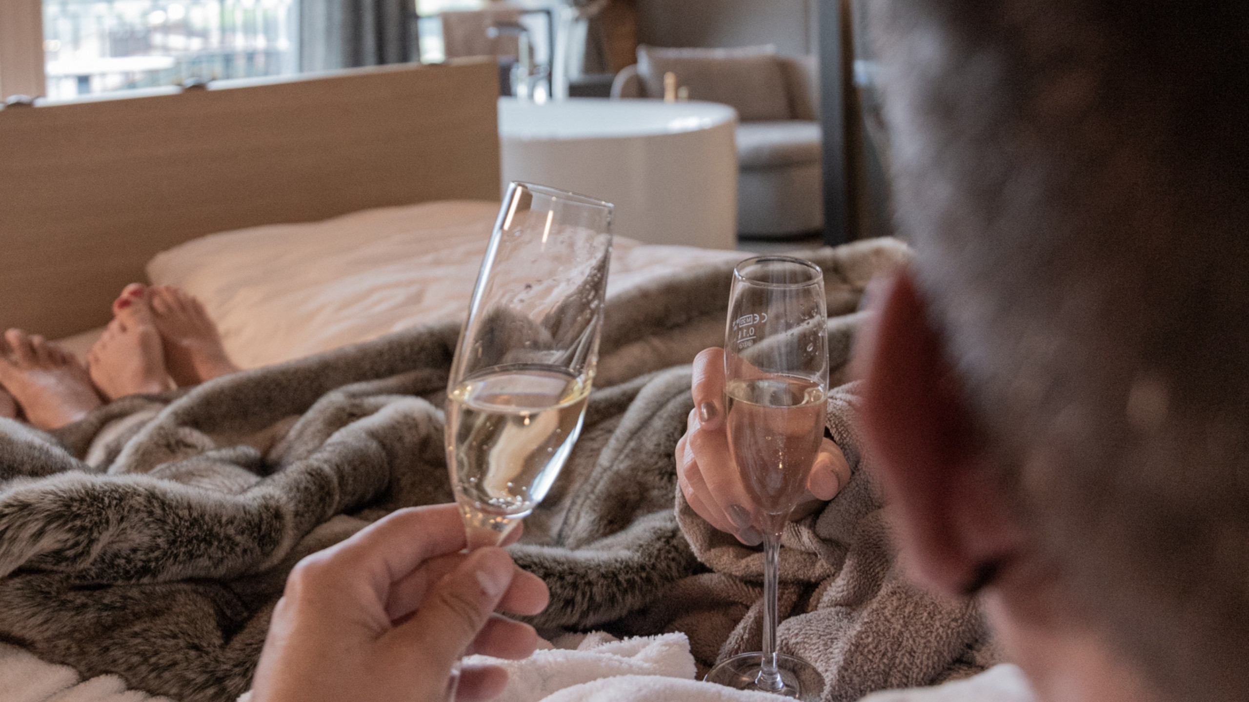 Baumhaus Zwei Personen stoßen mit Sektgläsern im Bett an, eine Decke umhüllt sie