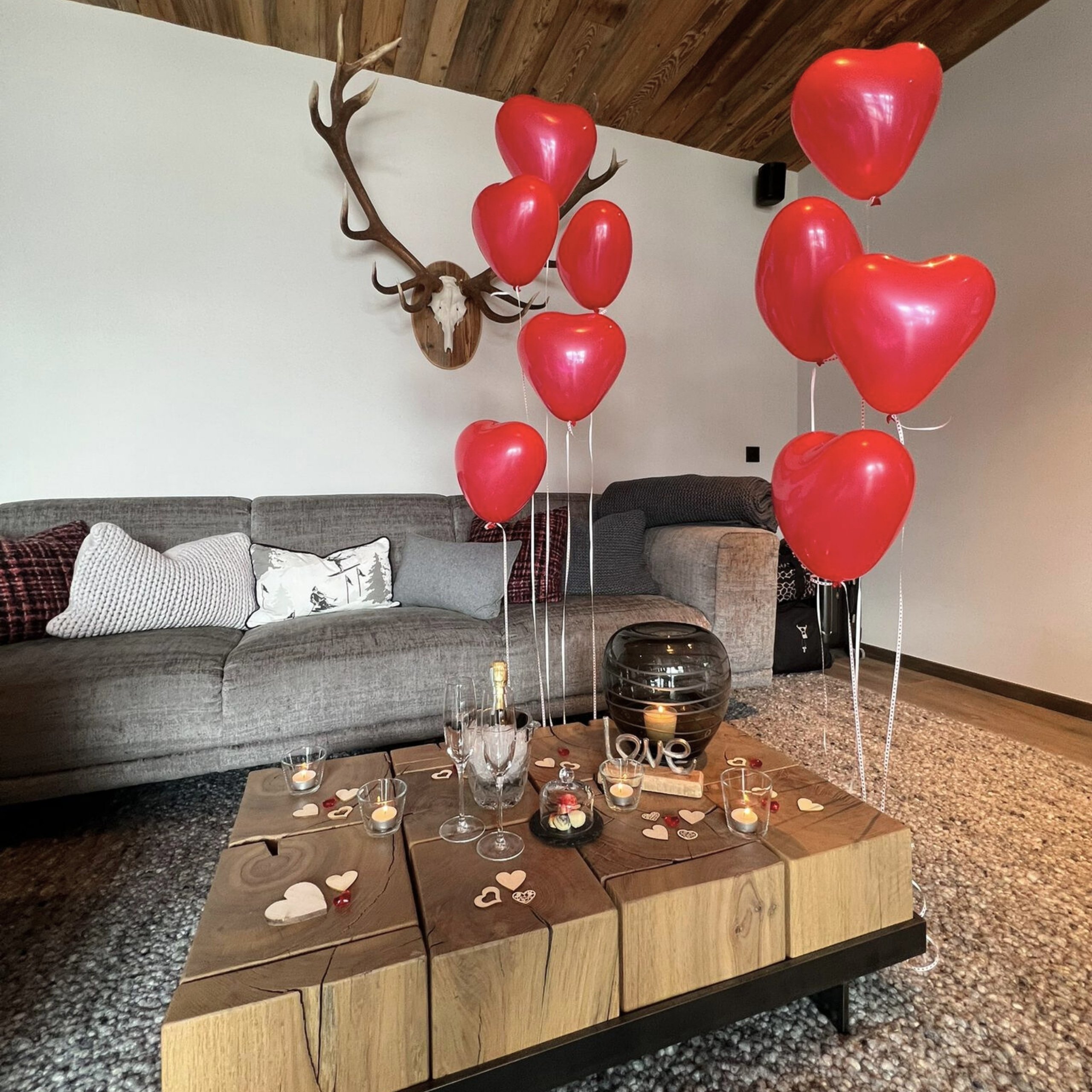 Baumhaus Wohnzimmer mit roter Herzluftballon-Dekoration und Holztisch mit Kerzen und Champagner
